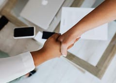 Two professionals shaking hands over a desk during a business agreement.