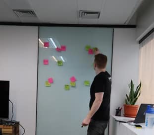 A team member stands in front of a whiteboard covered in colorful sticky notes, mapping out ideas and organizing a project plan during a strategy session.