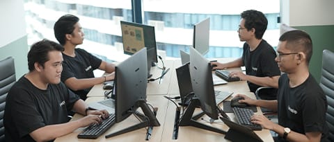 A group of IT professionals working collaboratively on desktop computers in an office environment, showcasing teamwork in software development