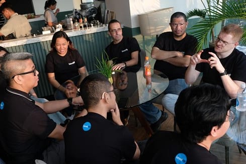 A group of LevelUp team members in black shirts sitting around a glass table, engaged in a casual discussion in a modern office space