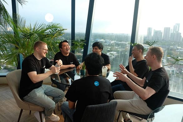 The LevelUp team seated around a table in a glass-walled rooftop room with a view of the city, smiling and engaged in casual conversation during an offsite planning session.