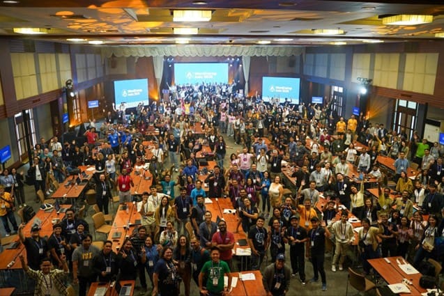 A wide-angle photo of the Contributor Day venue at WordCamp Asia 2025, filled with hundreds of attendees actively working in groups across large tables, showing the energy and scale of the open-source event.