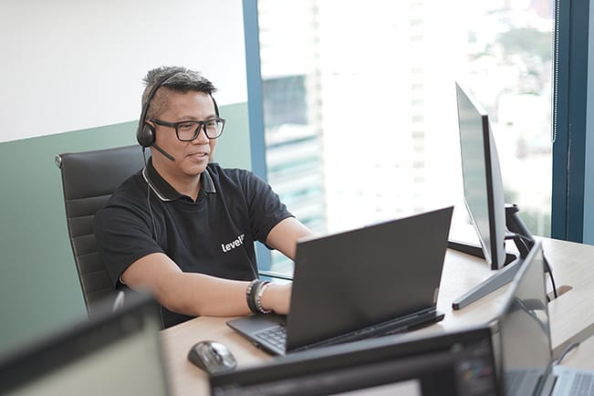 A LevelUp offshore Sales Development Representative wearing a headset, working on a laptop in a modern office setting.
