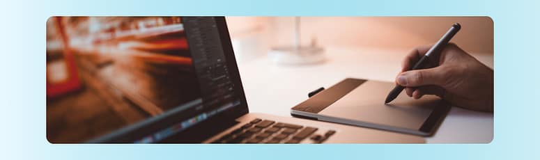 Designing Digital Assets Close-up of a person using a digital pen tablet beside a laptop, creating visual assets for graphic design projects.