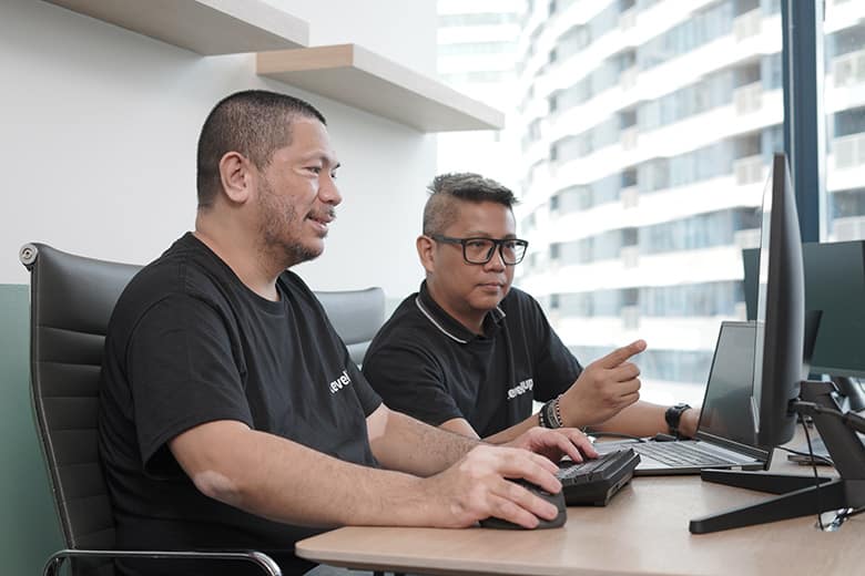 Two offshore software developers in LevelUp-branded shirts collaborate on a computer screen, discussing project strategies in a modern office.