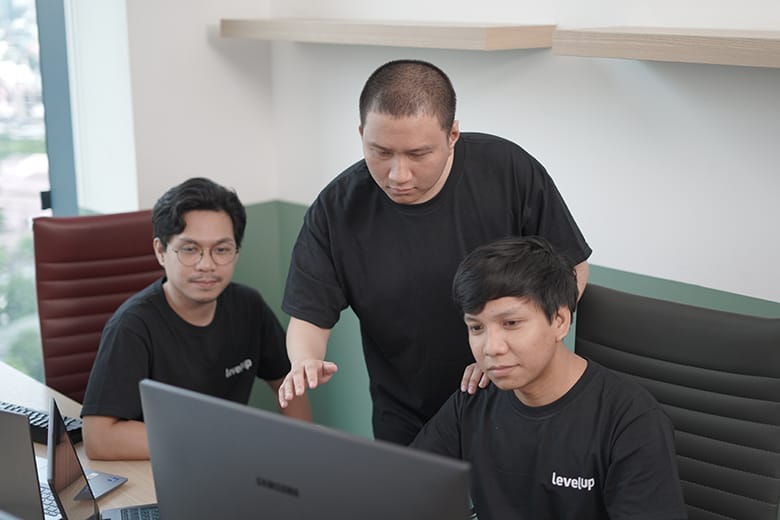 Three LevelUp team members collaborating around a computer during a discussion, highlighting a culture of support and teamwork.