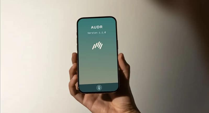Hand holding a smartphone showing the AUDR app (Version 1.1.0), representing the UK startup’s AI-powered mobile application.