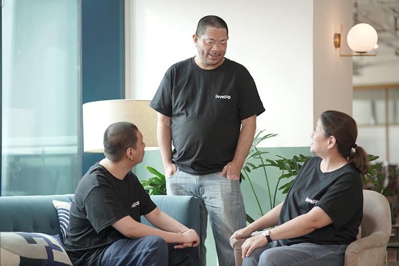 CSR_photo Three professionals having a conversation, with two seated on a couch and one standing nearby, engaging in discussion.