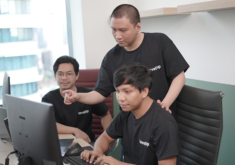 LevelUp Offshore Team Collaboration A group of LevelUp team members collaborating in an office, reviewing data on a computer screen, and discussing financial strategies while wearing branded company shirts.