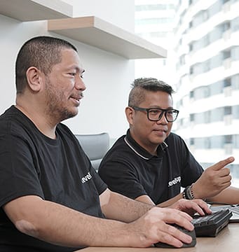 Two professionals collaborating in an office, with one pointing at a computer screen while discussing.