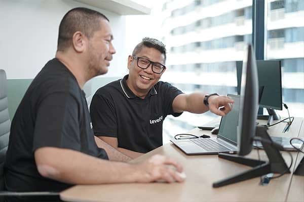 LevelUp team members reviewing work on a computer, with one pointing to the screen and smiling in a collaborative office environment.