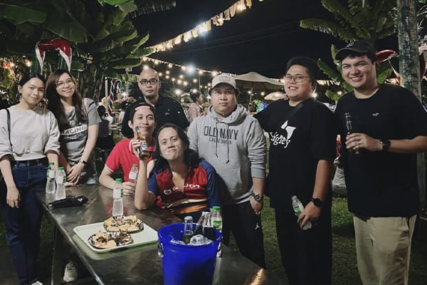 LevelUp team members enjoying a night out in a festive outdoor setting, holding drinks and posing for a photo in front of string lights.