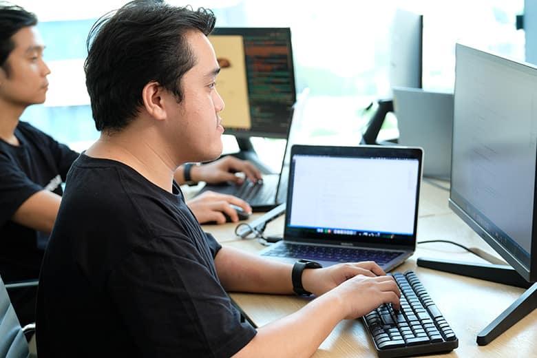 Focused team members working on their laptops and monitors in a collaborative office setting, showcasing productivity and technical expertise.