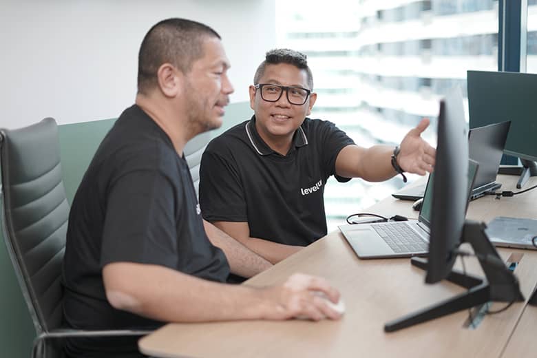 Two professionals collaborating in an office, with one pointing at a computer screen while discussing.