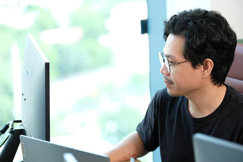 A professional in glasses works on a computer in a bright office environment, looking focused.